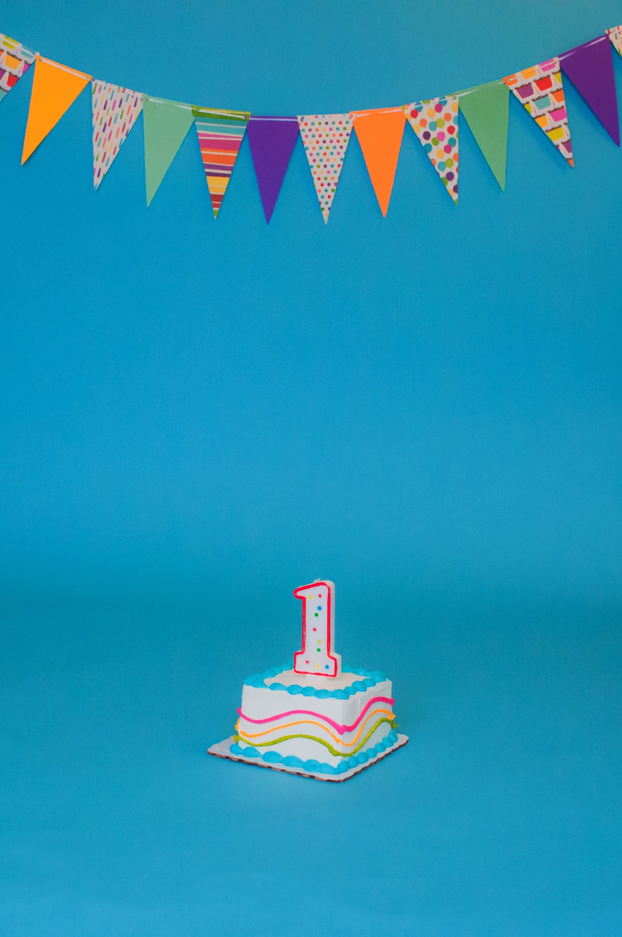 Tort urodzinowy z jedną świeczką o numerze 1. Całość na niebieskim tle