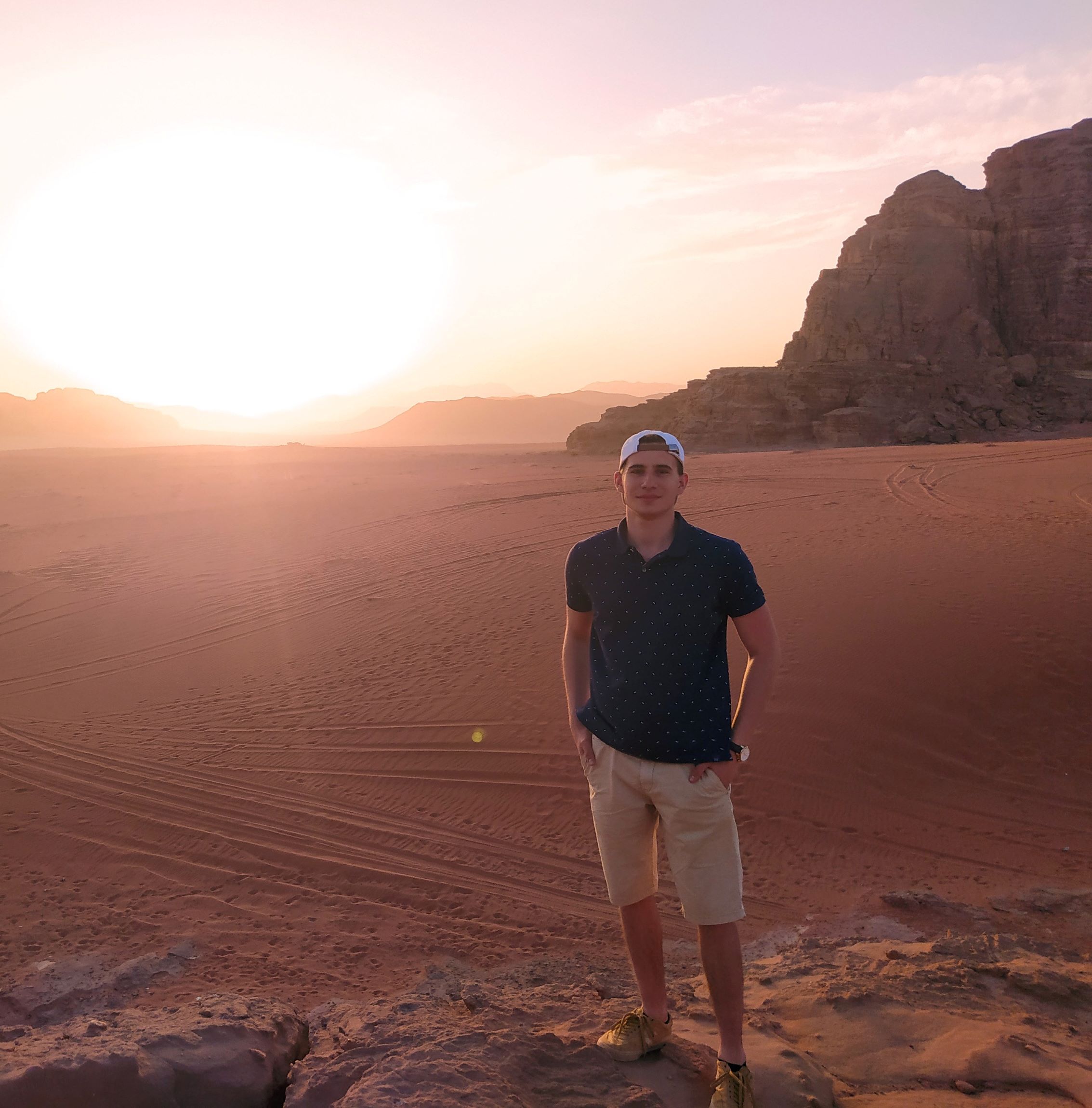 mężczyzna stoi na skale na pustyni, w tle pustynia i zachód słońca