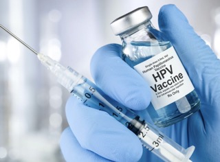 Zdjęcie przedstawia dłoń ubraną w niebieską lateksową rękawicę. Dłoń trzyma strzykawkę i fiolkę szczepionki przeciwko HPV