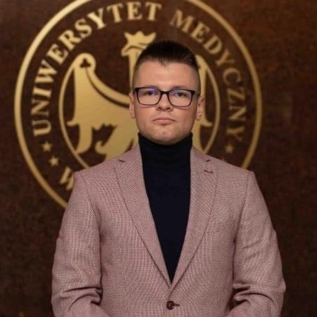 młody mężczyzna stoi na tle godła Uniwersytetu Medycznego w Lublinie