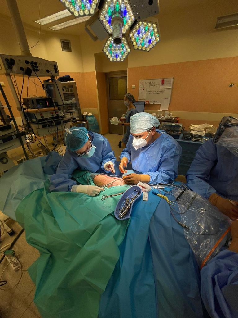 Zdjęcie z sali operacyjnej, trzej lekarze pochyleni nad pacjentem, widać pole operacyjne