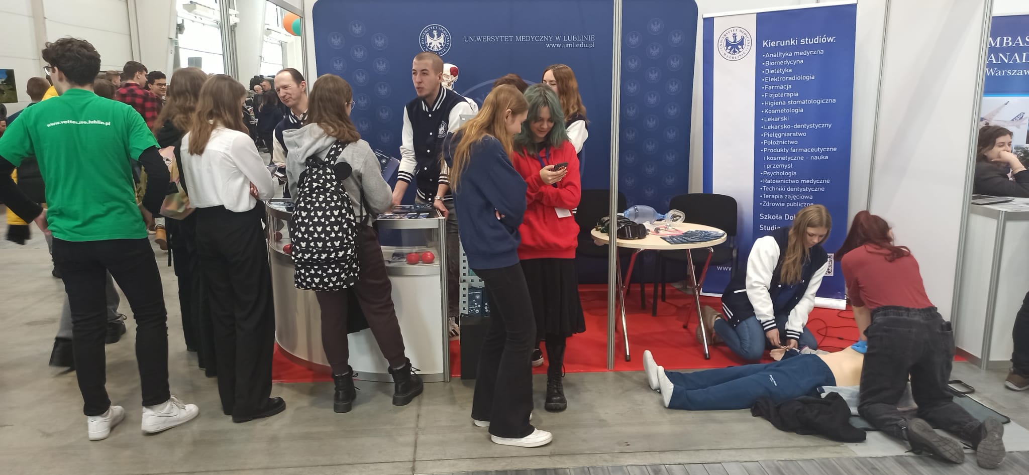 Stoisko na targach edukacyjnych, przedstawiciele uniwersytetu medycznego w Lublinie rozmawiają z zainteresowanymi licealistami
