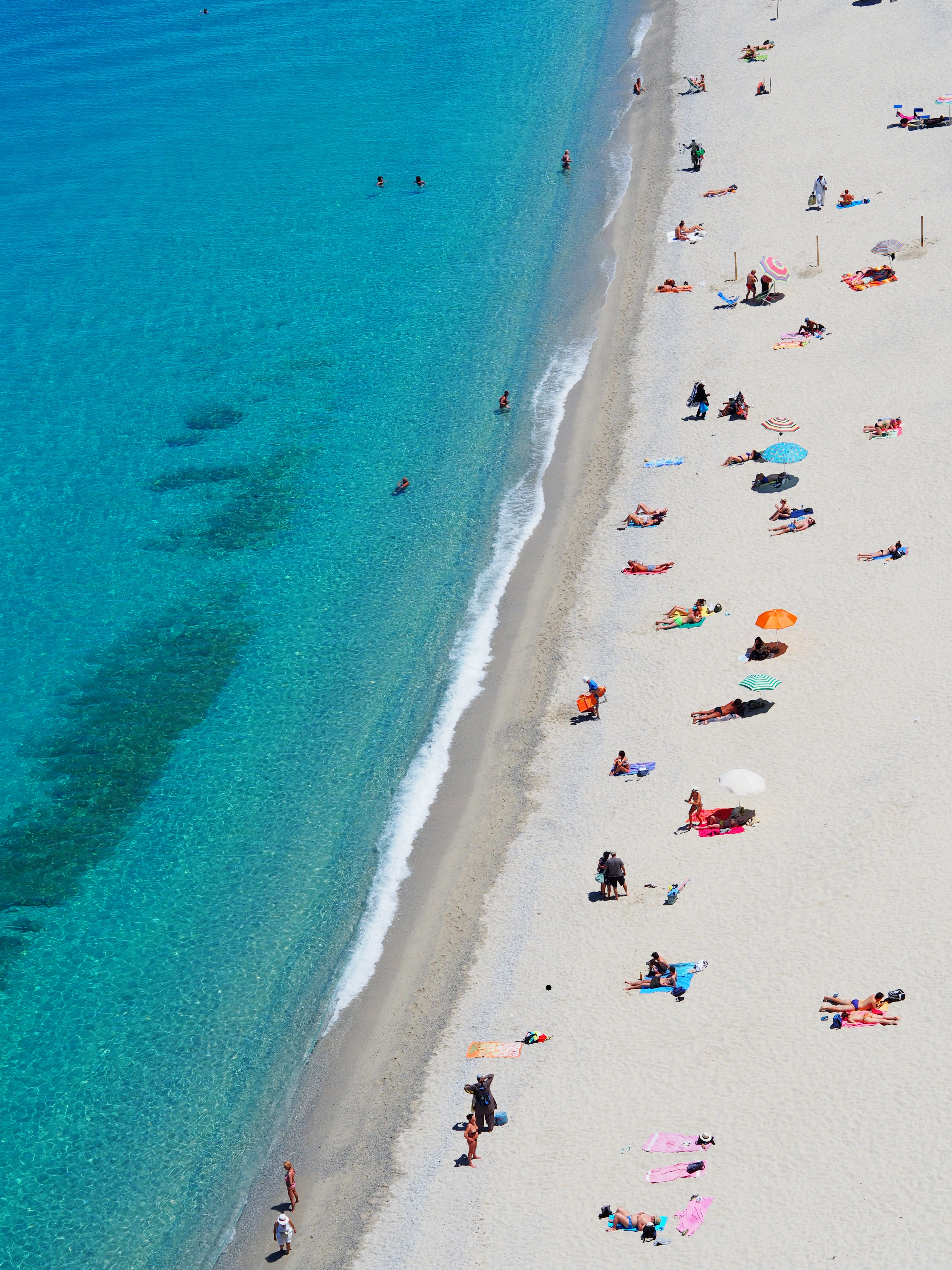 Zdjęcie przedstawia plażę i ocean, na plaży opalają się ludzie.