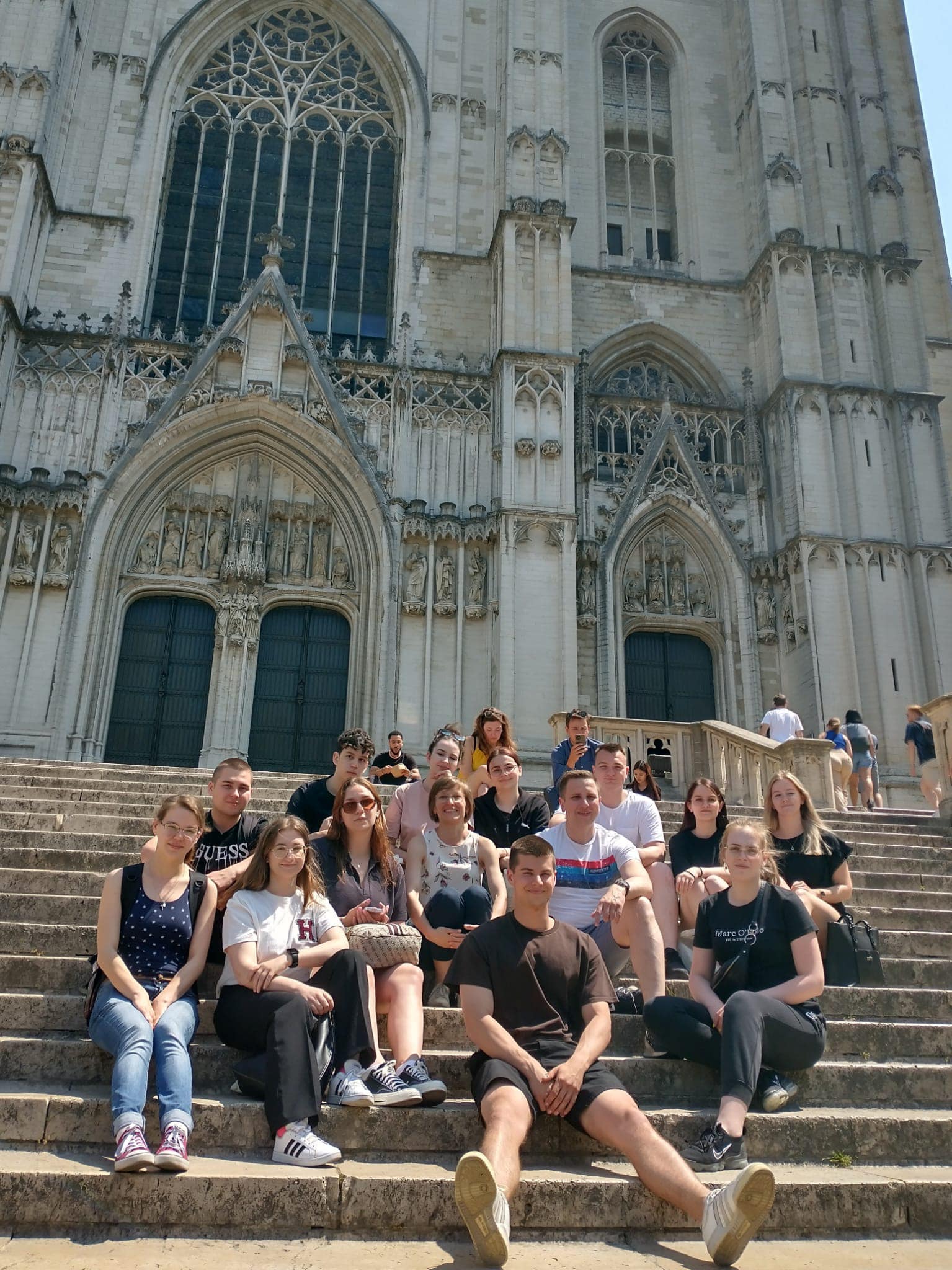 uczestnicy wycieczki siedzą na schodach przed katedrą w Brukseli