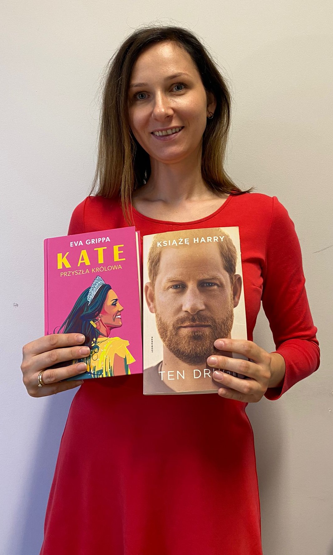 kobieta stoi, trzyma w rękach dwie ksiązki, jedna o książnej Kate, druga o księciu Harrym