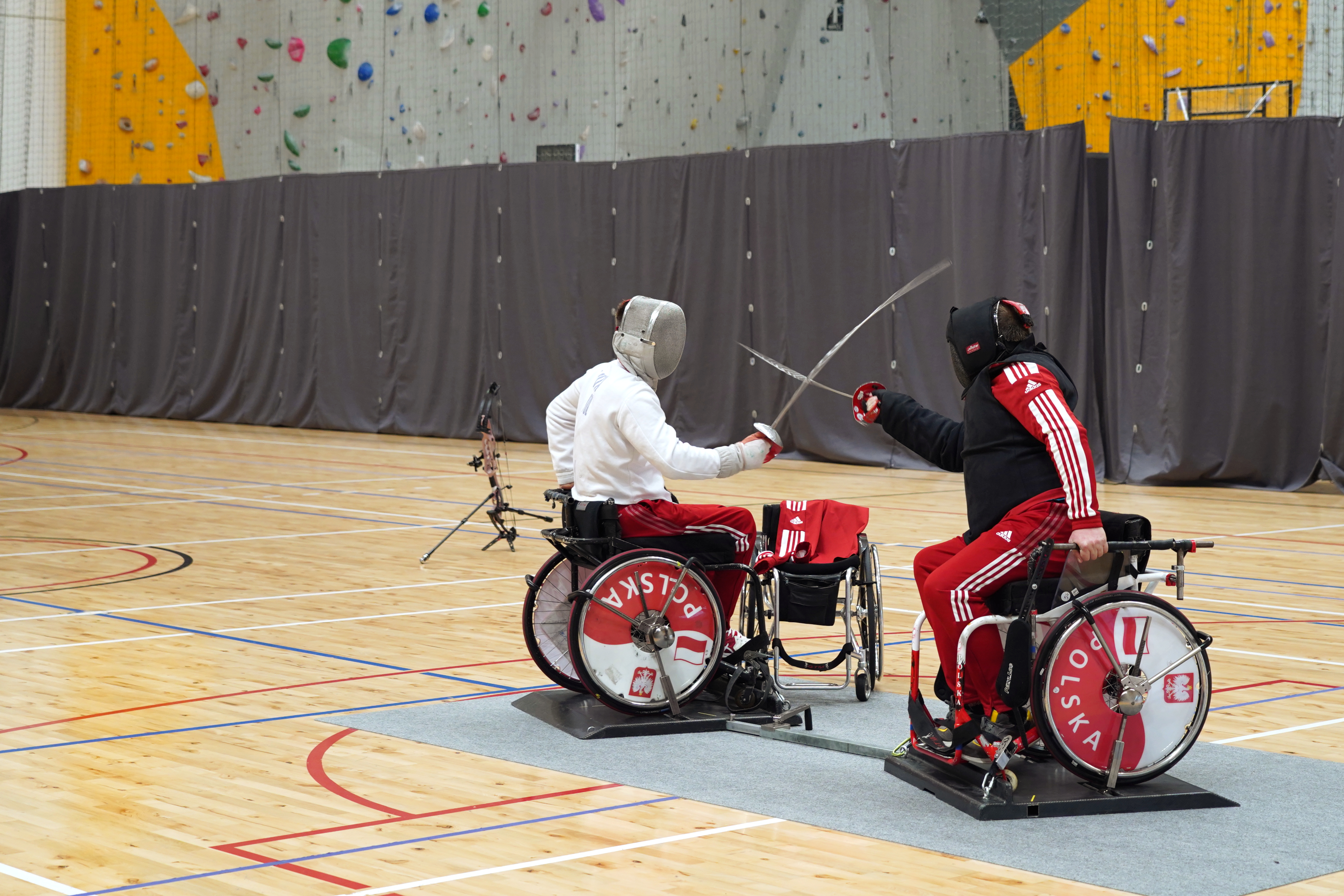 Dwóch sportowców prezentuje pokaz szermierki. Sportowcy poruszają się na wózkach inwalidzkich