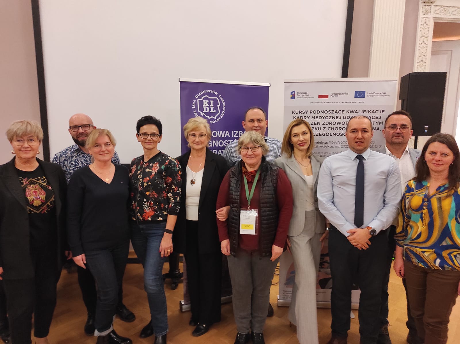 Organizatorzy i prelegenci seminarium stoją obok siebie. W tle stoją rollupy.