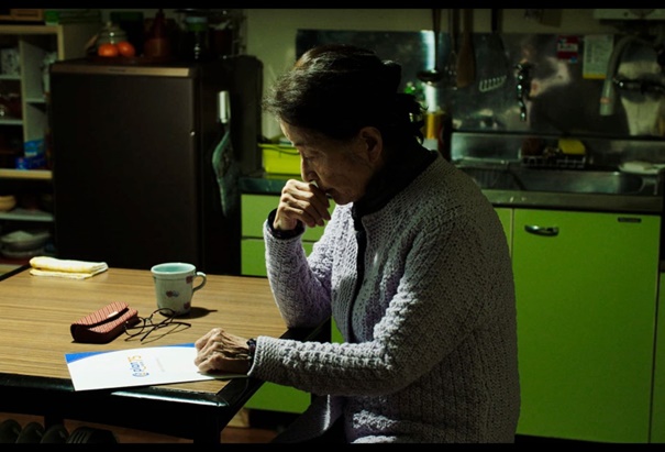 Old Japanese person sits by the counter reading some paper