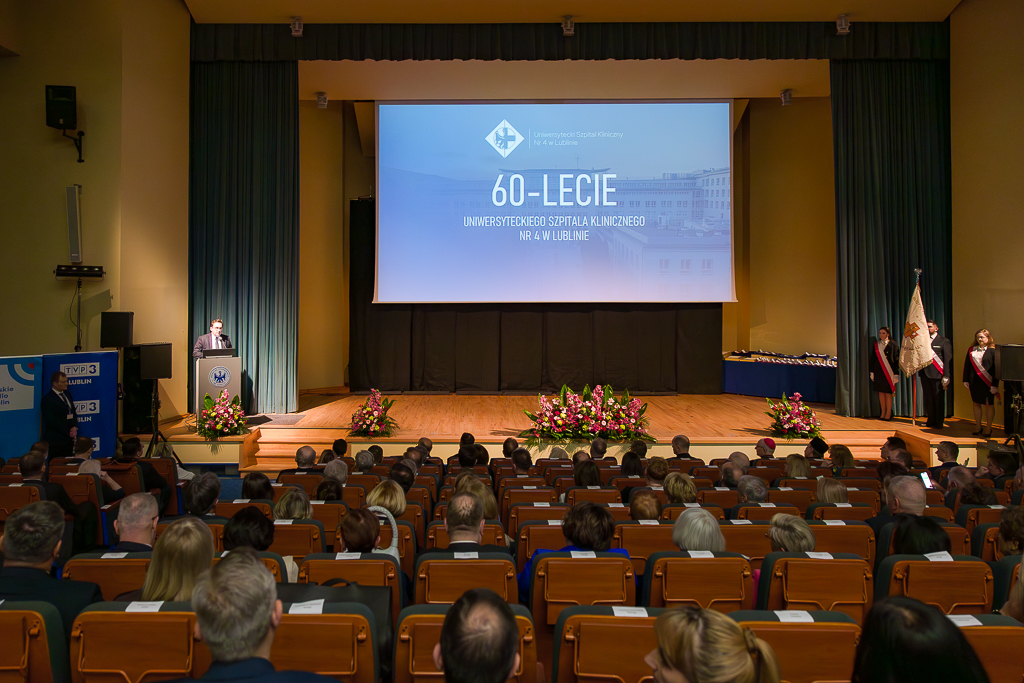 aula uniwersytecka, wszystkie miejsca zajęte, mężczyzna na mównicy przemawia a w centrum zdjęcia plansza 60-lecie Uniwersyteckiego Szpitala Klinicznego nr 4 