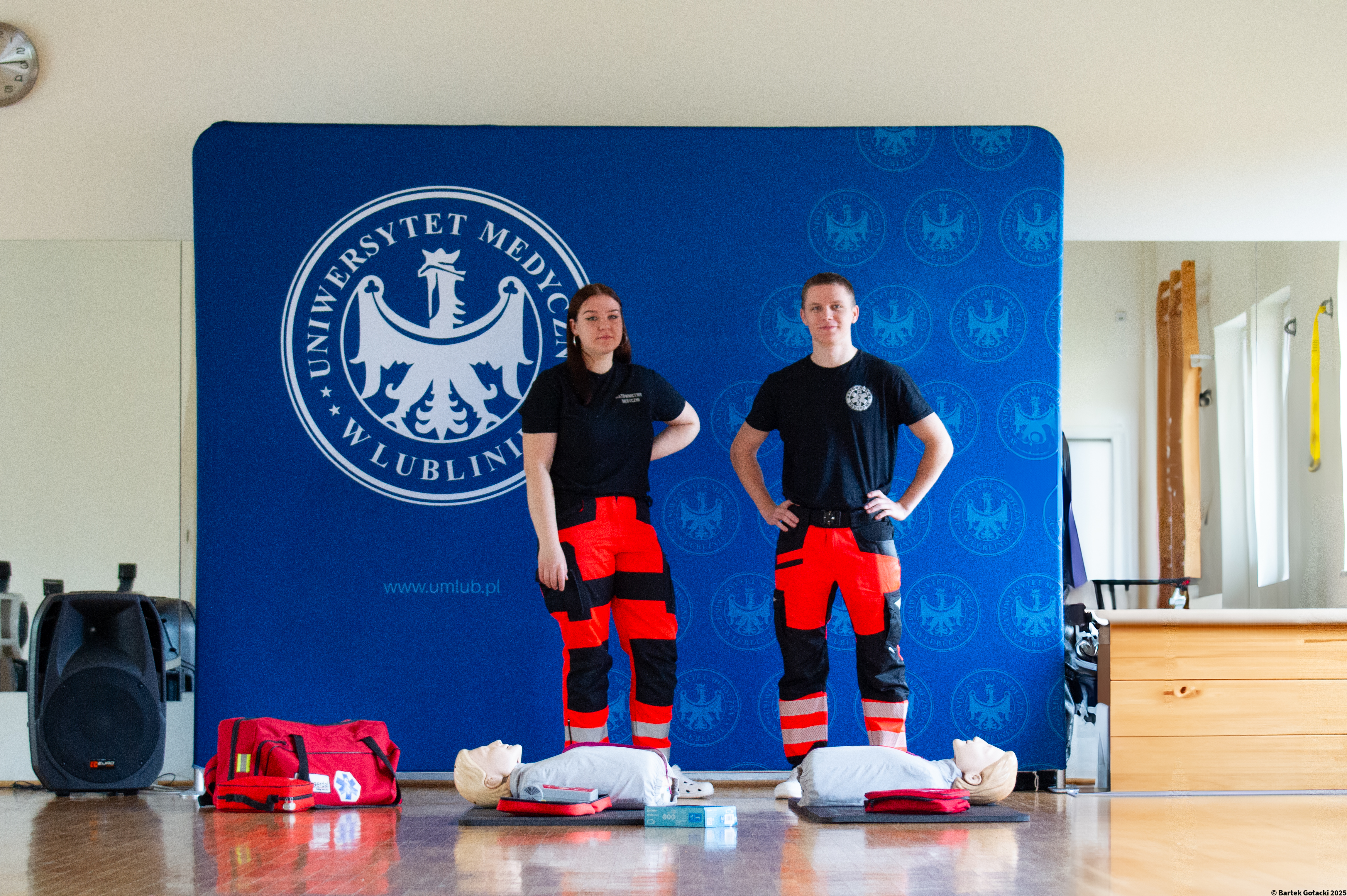 studenci z SKN Ratownictwa Medycznego stoją na tle ścianki uniwersyteckiej