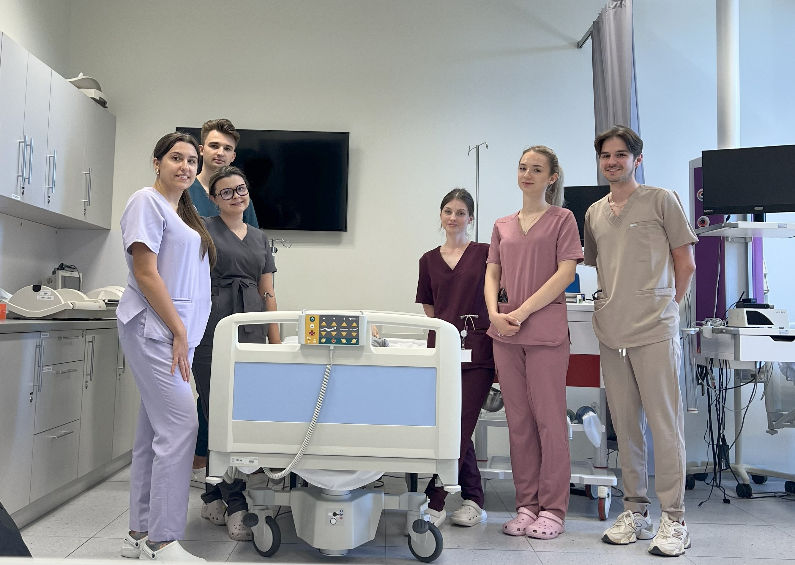studenci w scrubsach stoją przy łóżku szpitalnym