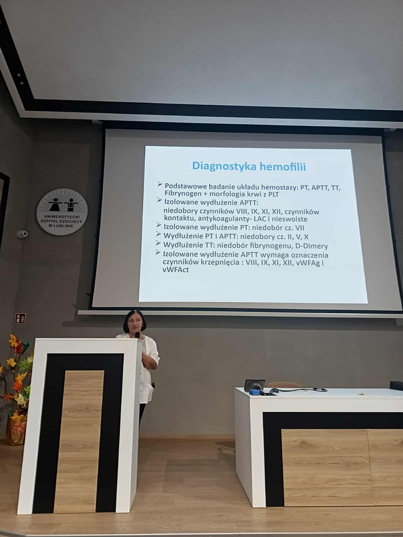 Wykładowca wygłasza wykład o diagnostyce hemofilii - w tle slajd z prezentacji