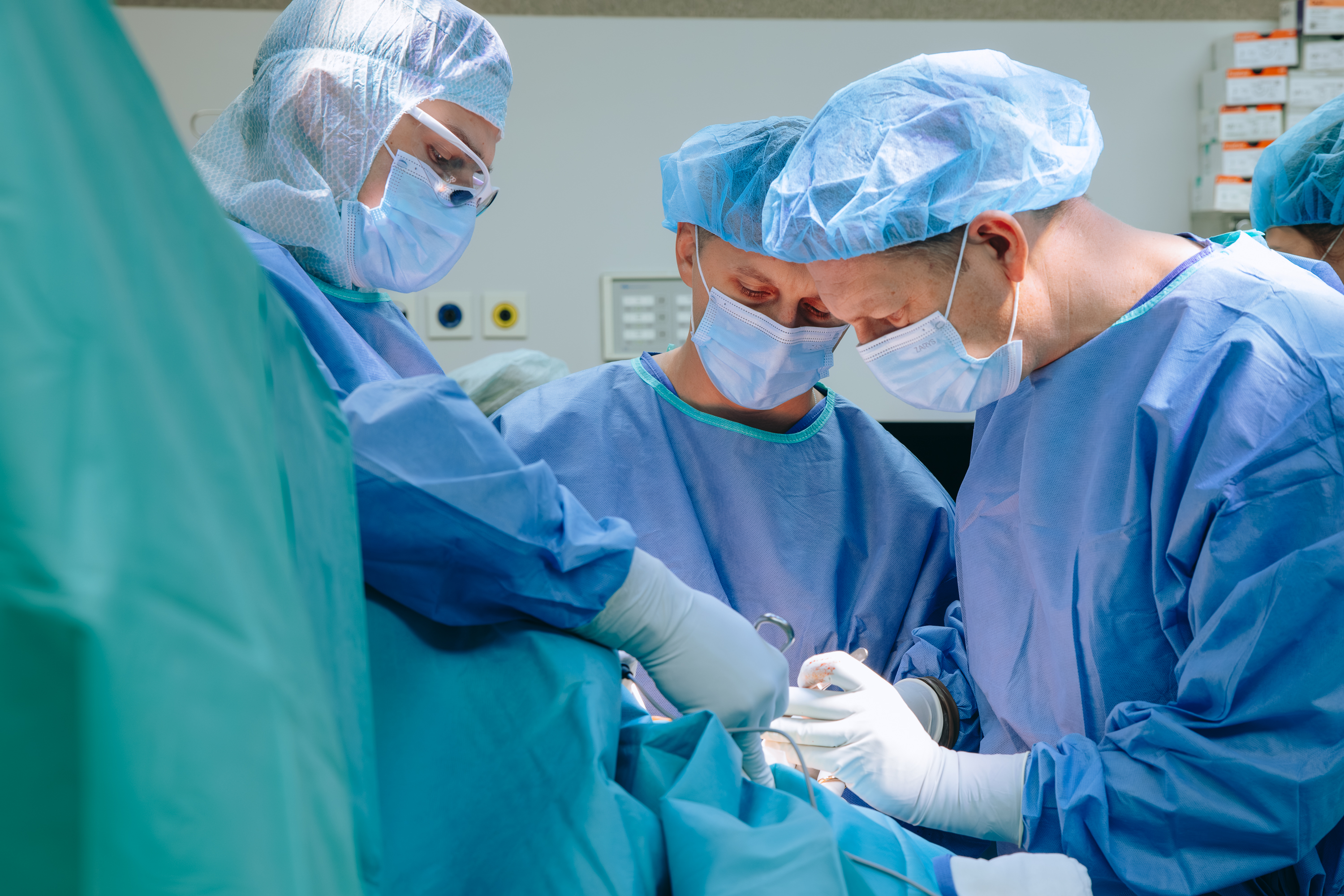 trzech chirurgów przy stole operacyjnym - przygotowują się do cięcia